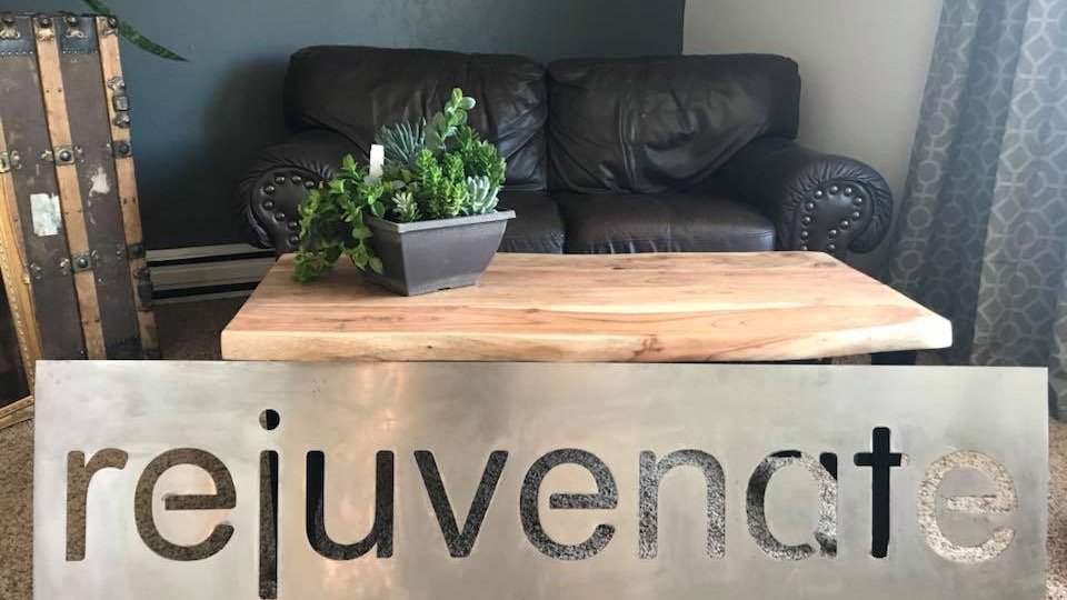 The Rejuvenate salon space — metal sign, live-edge wood table, leather couch